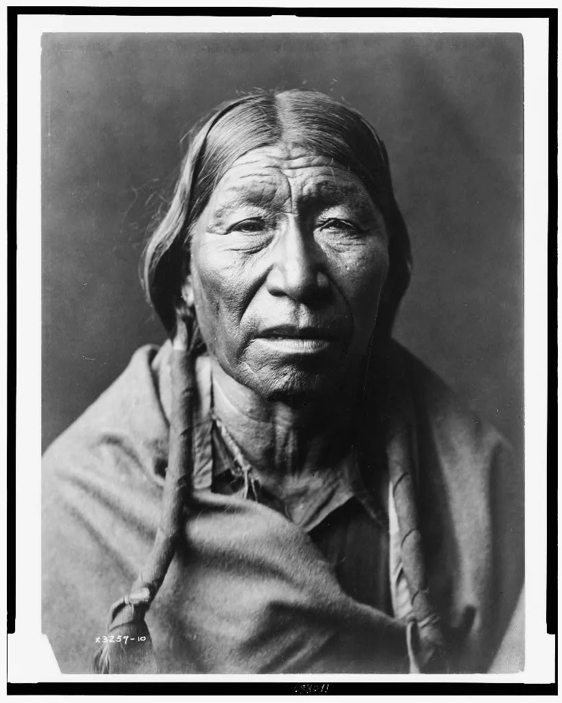 [Cheyenne male, facing front, hair in wrapped braids, blanket around…, 1910